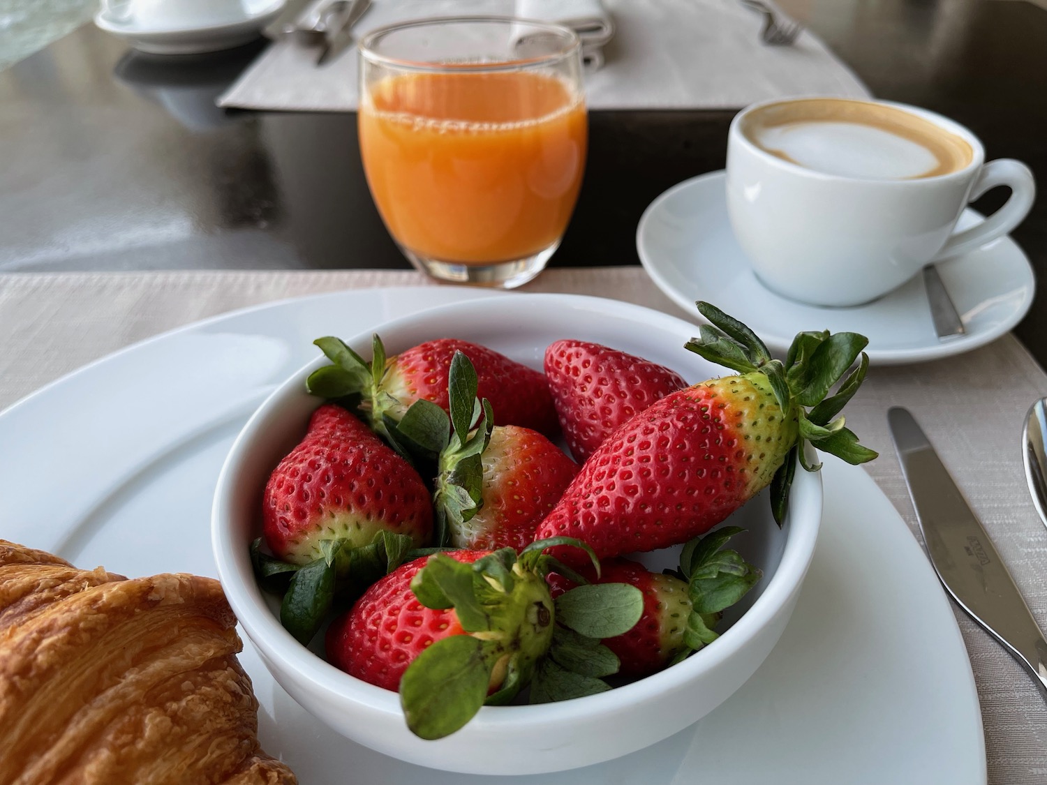 a bowl of strawberries and a croissant on a plate