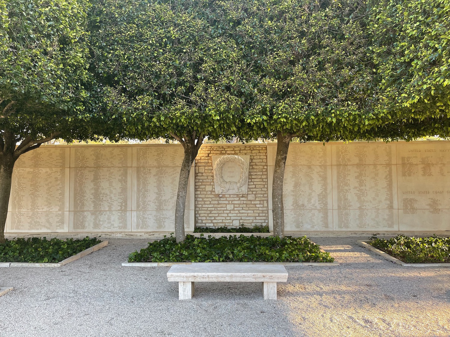 a stone bench and trees in front of a wall