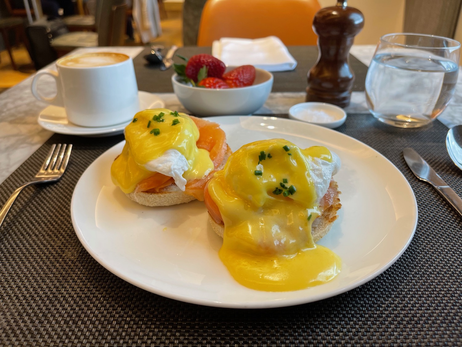 a plate of eggs benedict with a cup of coffee and strawberries