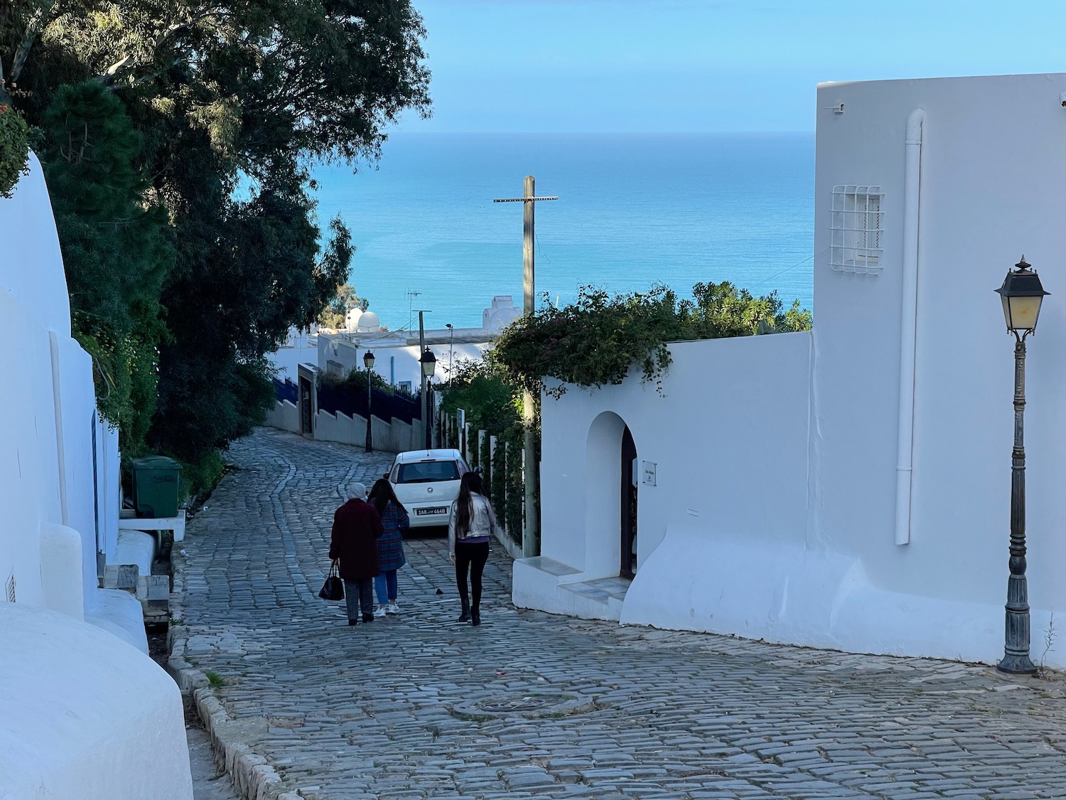 people walking on a cobblestone road with white buildings and trees