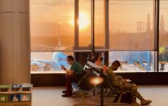 people sitting in a waiting area with a large window and a plane in the background