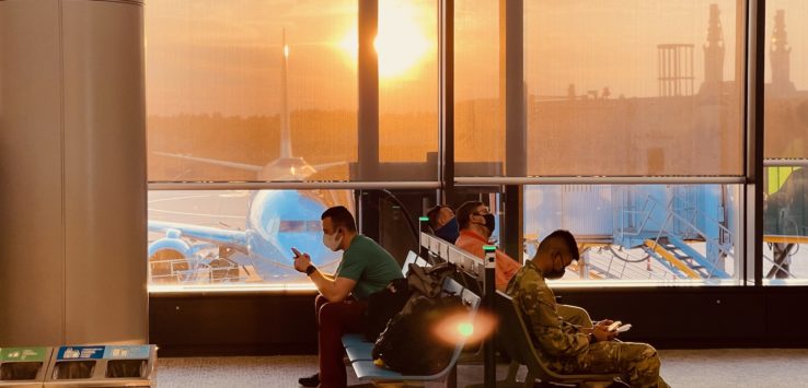 people sitting in a waiting area with a large window and a plane in the background
