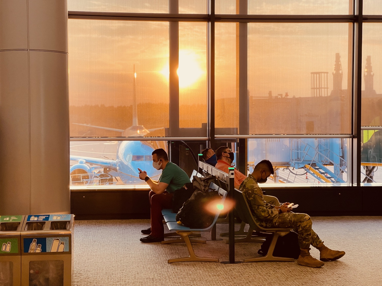 people sitting in a waiting area with a large window and a plane in the background