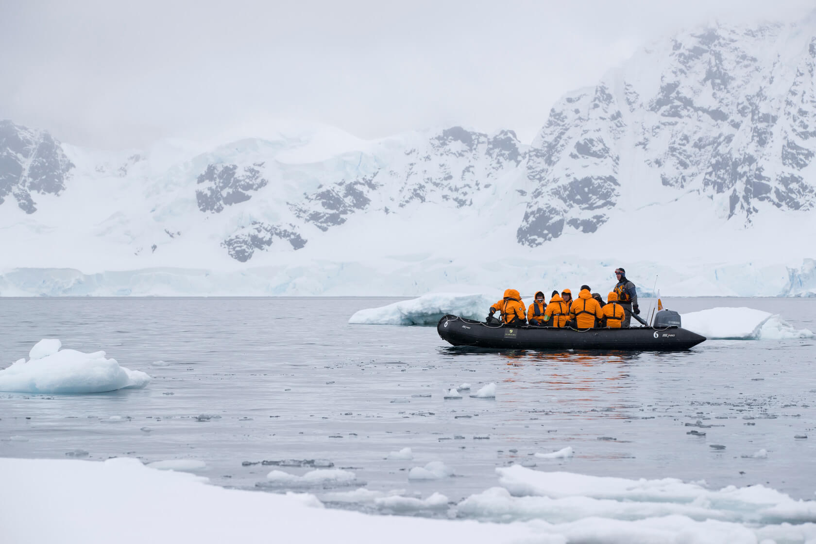 a group of people in a boat in the water with snow covered mountains