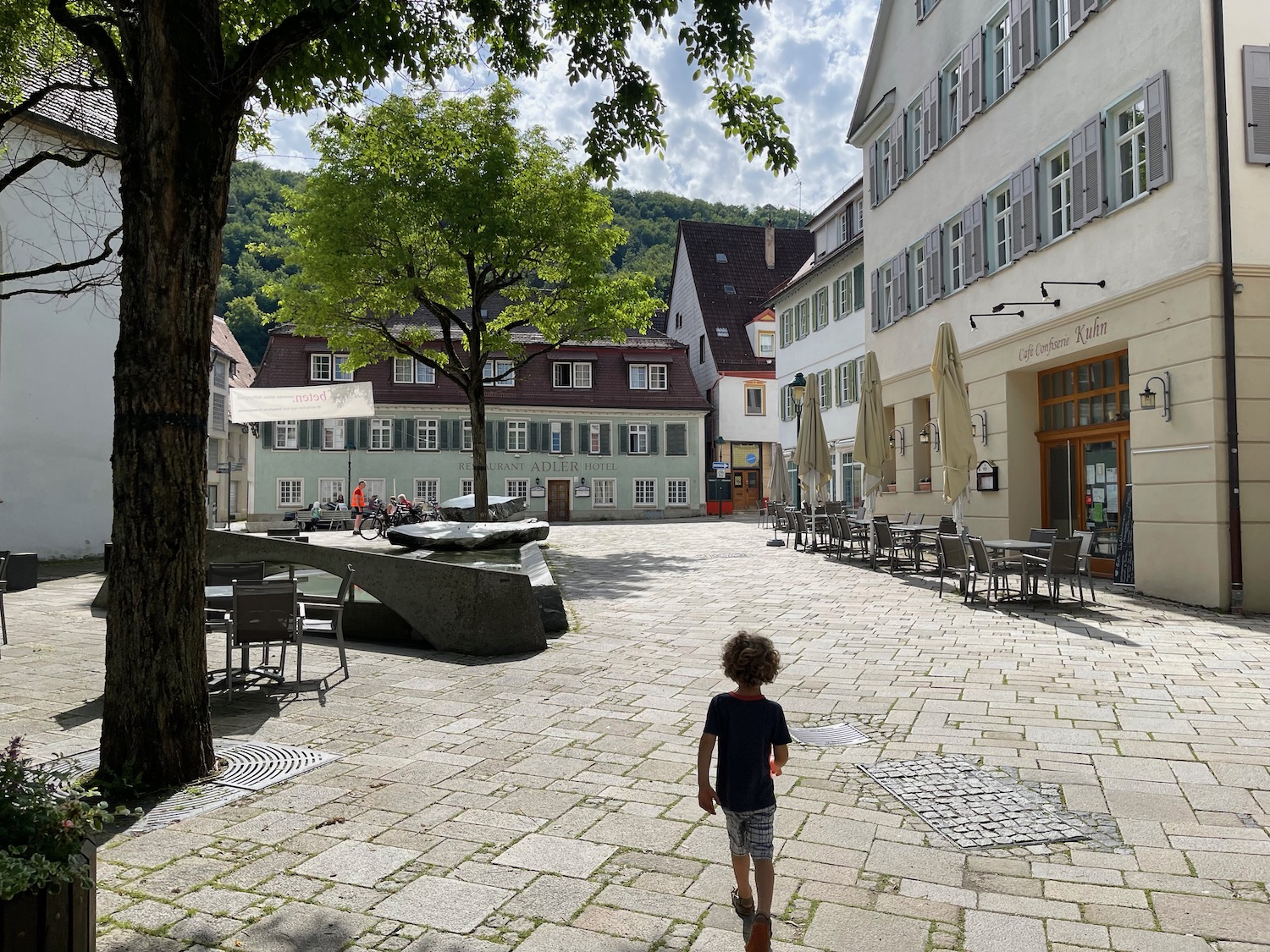 a child walking on a stone path with tables and chairs in front of buildings