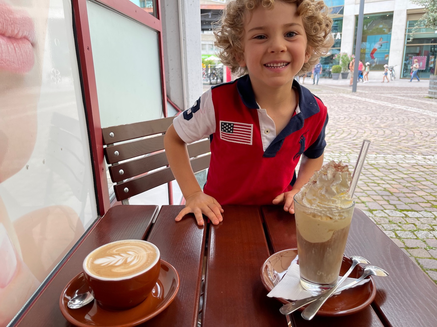 a boy sitting at a table with a cup of coffee and a drink