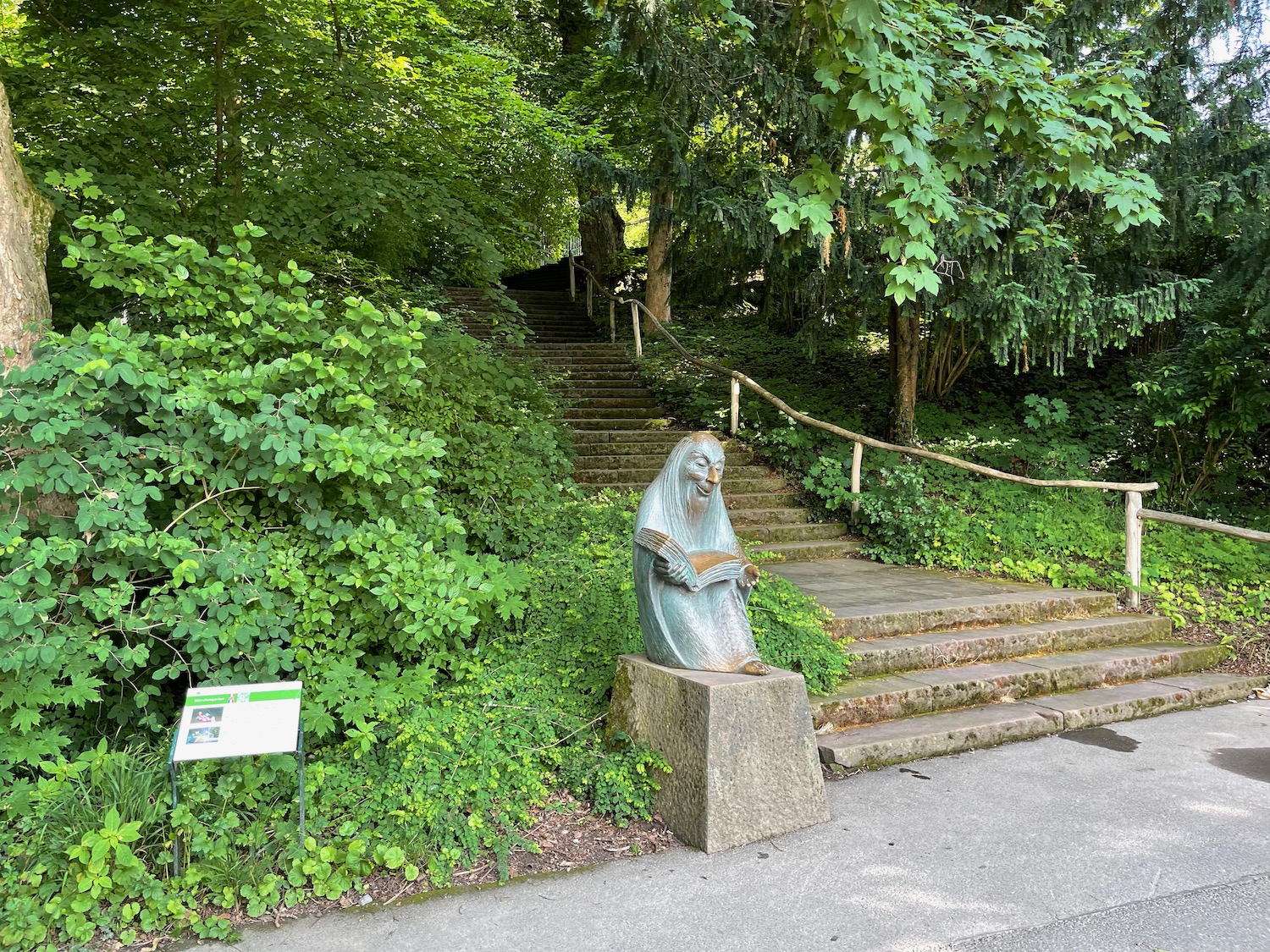 a statue of a woman sitting on a stone pedestal in a park