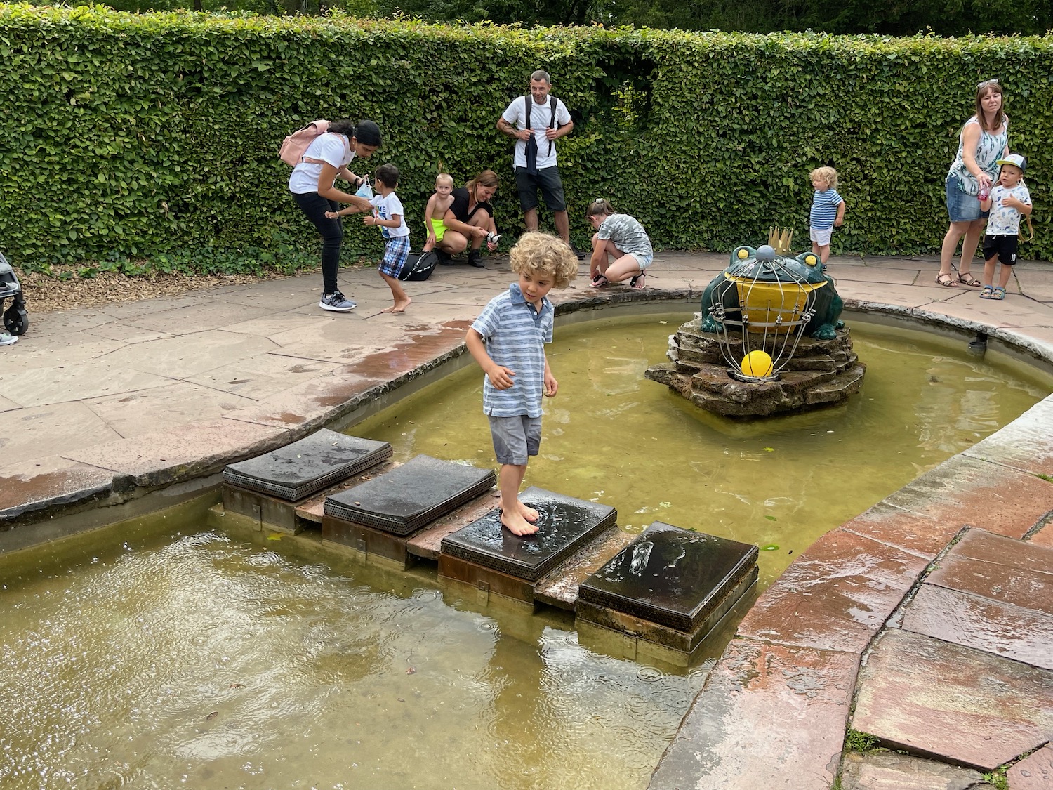 a boy standing on a small pond with people around