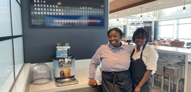 two women standing next to a coffee machine
