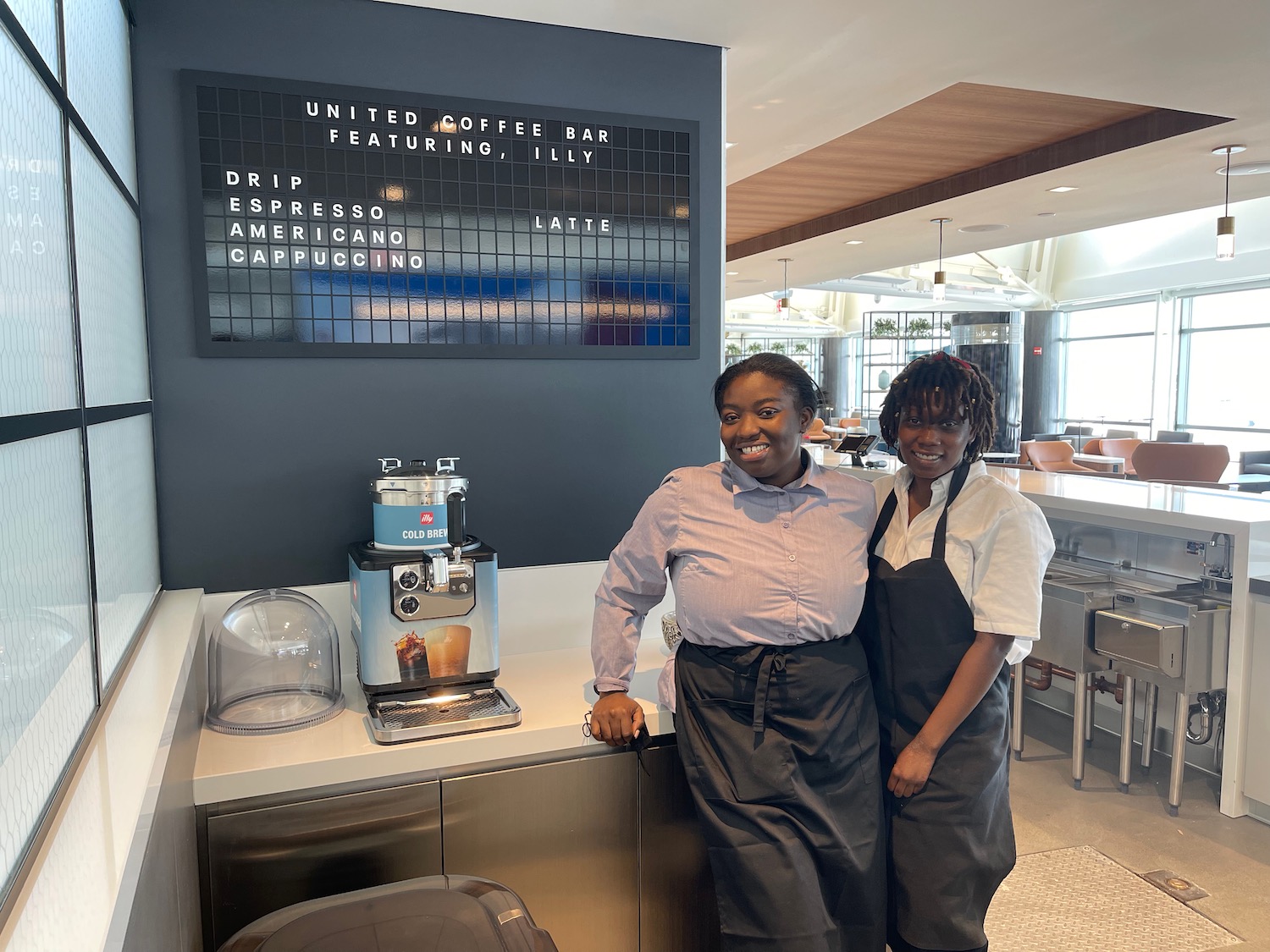 two women standing next to a coffee machine