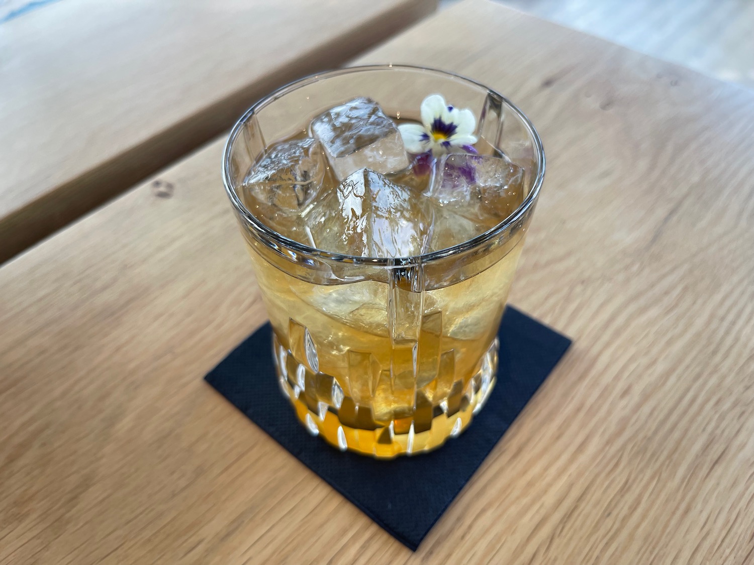 a glass of liquid with ice and a flower on a coaster