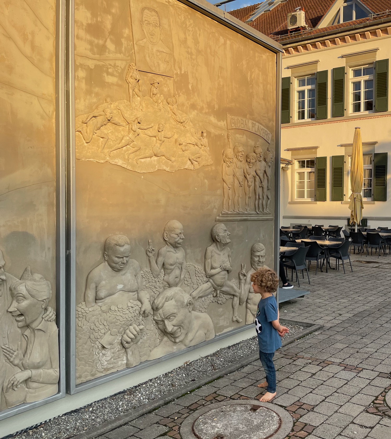 a child standing in front of a wall with a sculpture of people