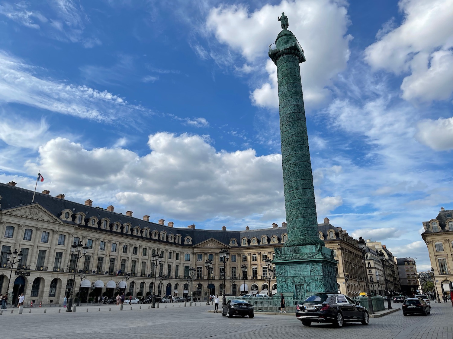 a tall green pillar in a plaza with cars and buildings