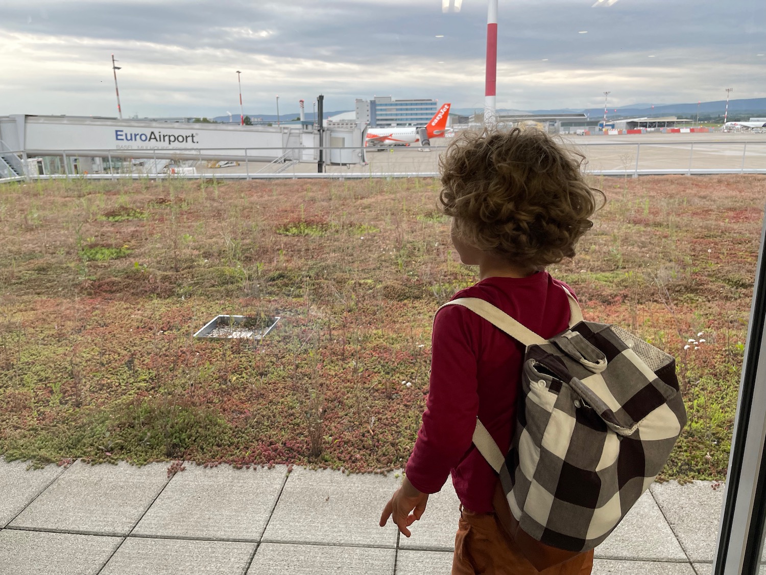 a child standing on a sidewalk looking at an airplane