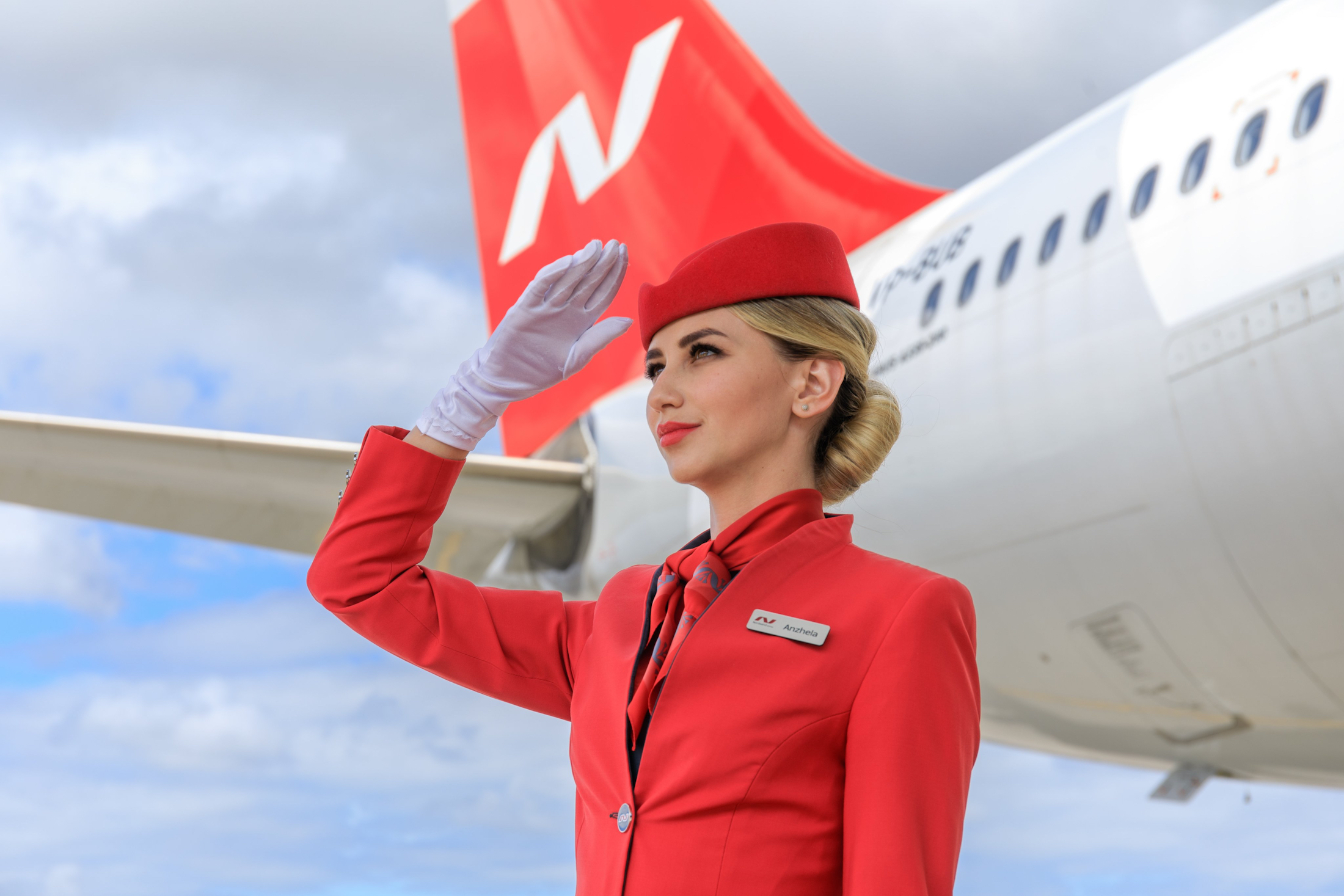 a woman in red uniform saluting with a plane in the background