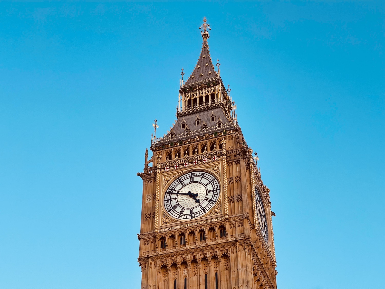 a clock tower with a pointy roof with Big Ben in the background