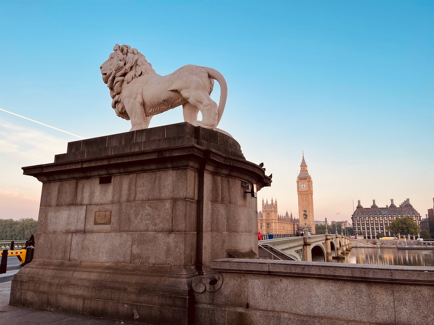 a statue of a lion on a stone wall with a clock tower in the background