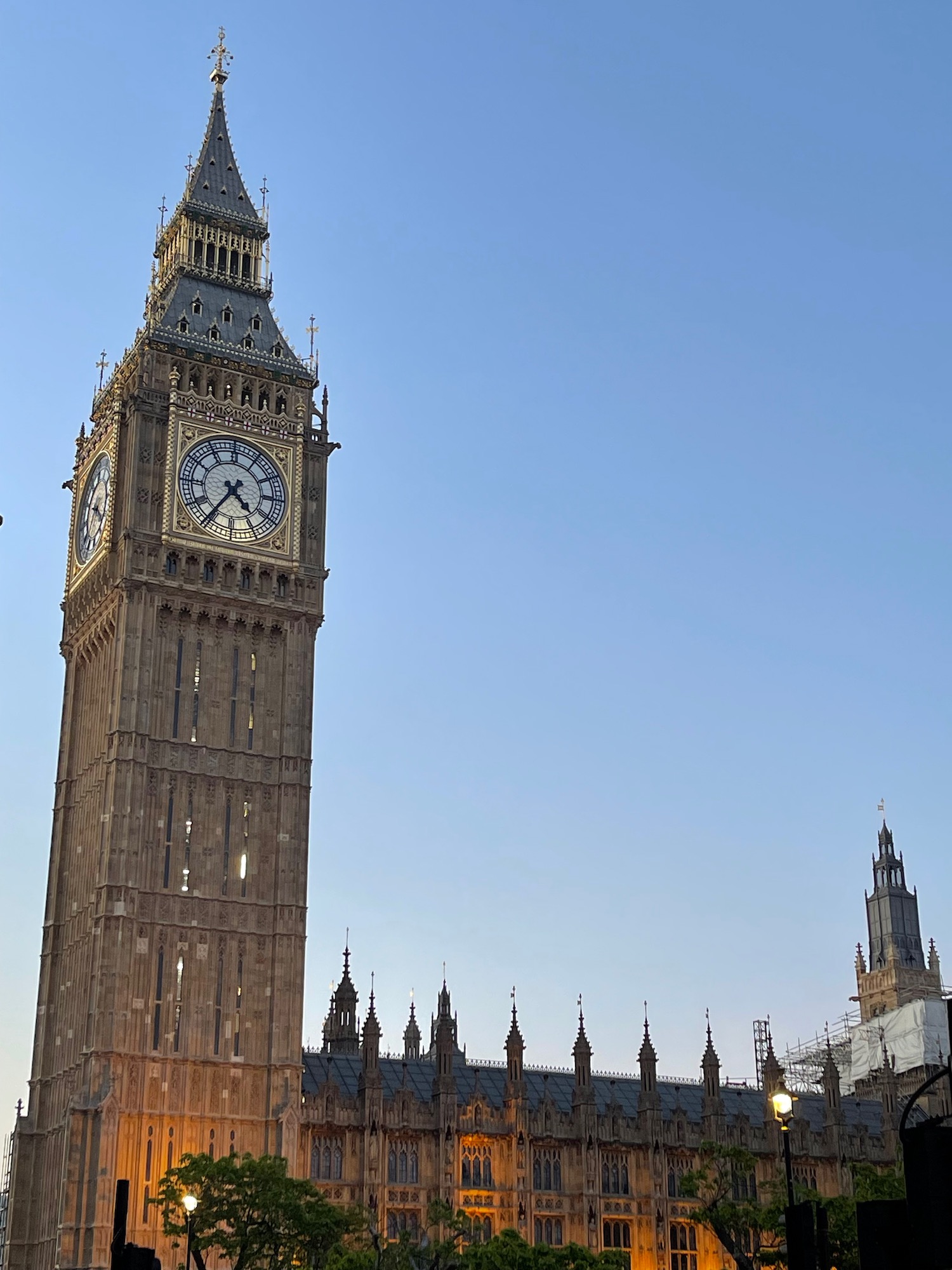 a clock tower with a pointed top with Big Ben in the background