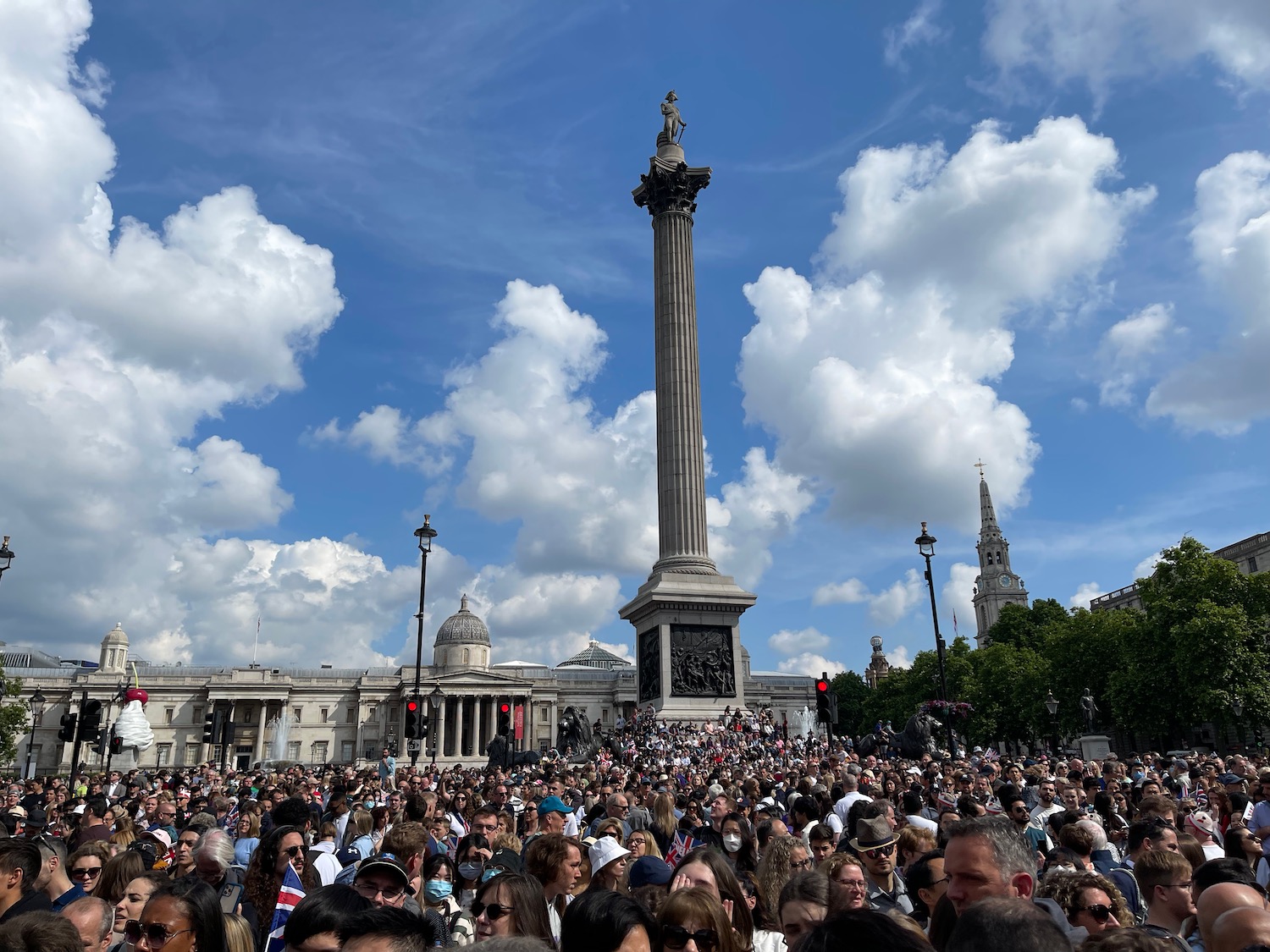 a large group of people in front of a tall monument with Trafalgar Square in the background