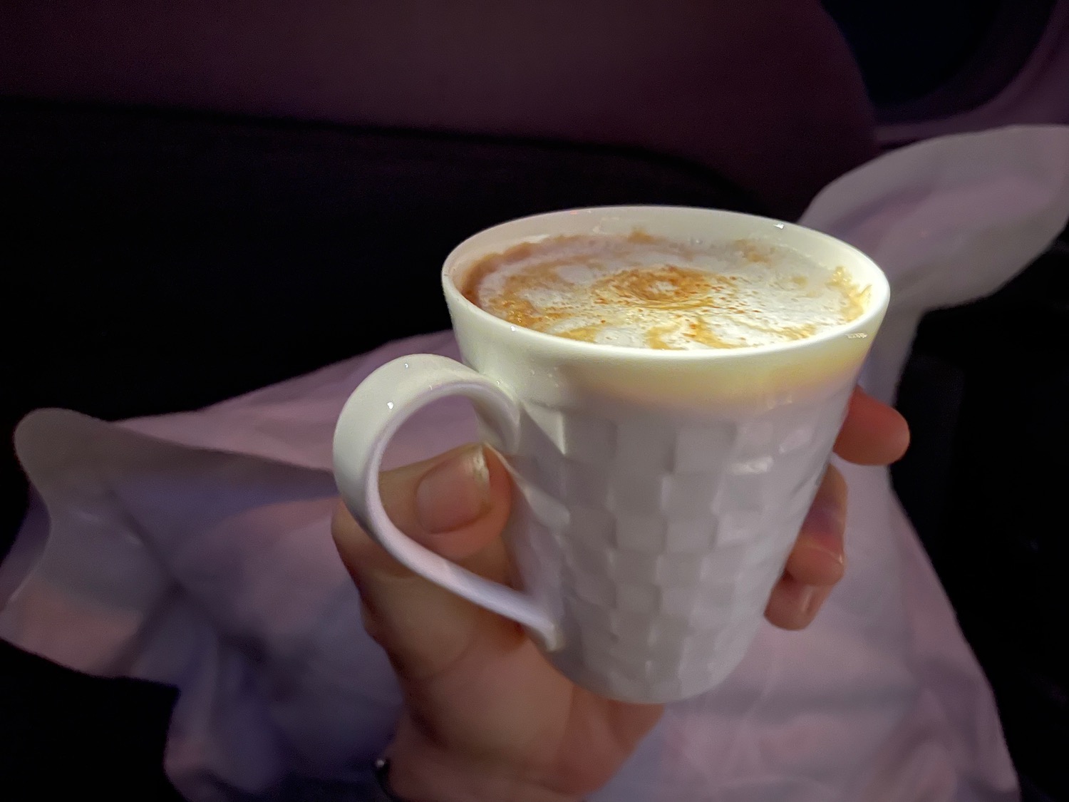 a hand holding a white cup with a brown foamy liquid