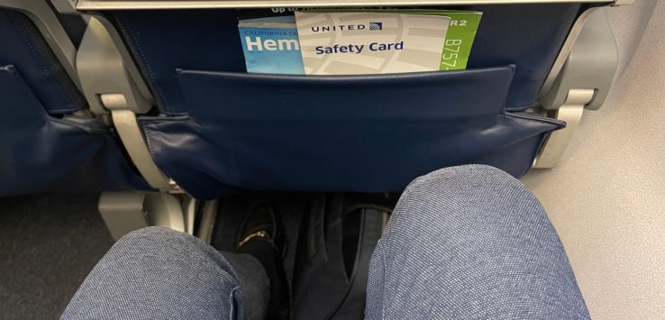 a person's legs in a seat with a safety card in the pocket