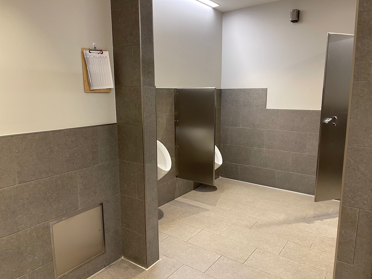 a bathroom with urinals and grey tile walls