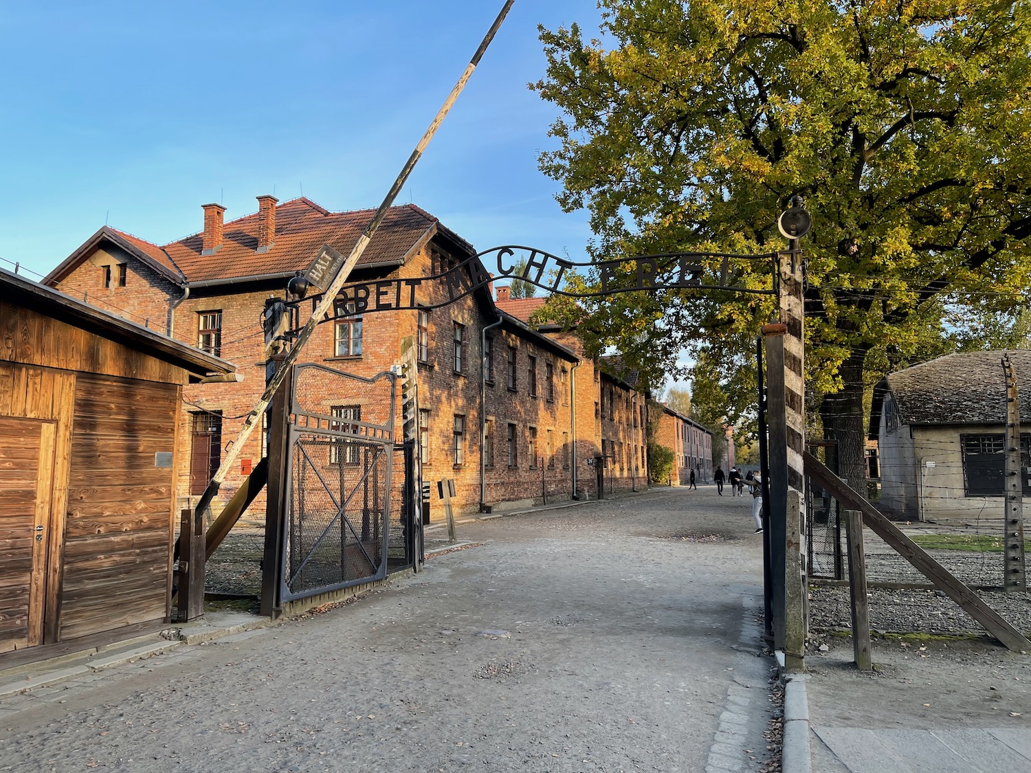 a brick buildings with a gate and trees with Auschwitz concentration camp in the background