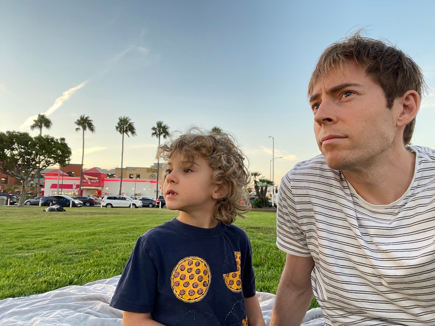 a man and child sitting on a blanket in a park