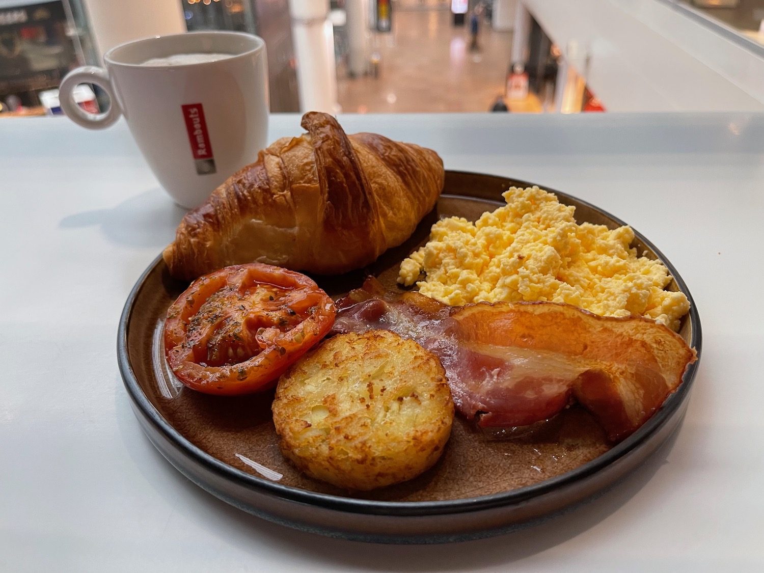 a plate of breakfast with bacon eggs and croissant