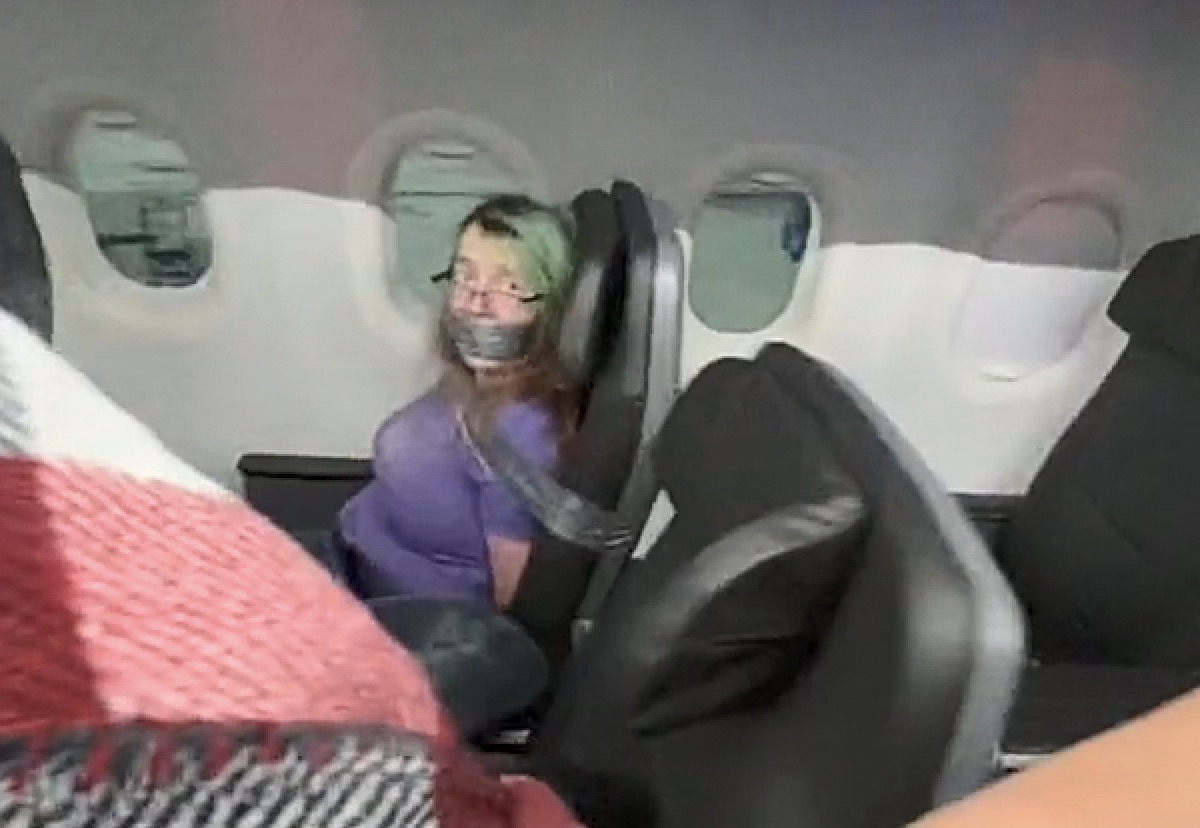 a woman with duct tape on her face sitting in an airplane