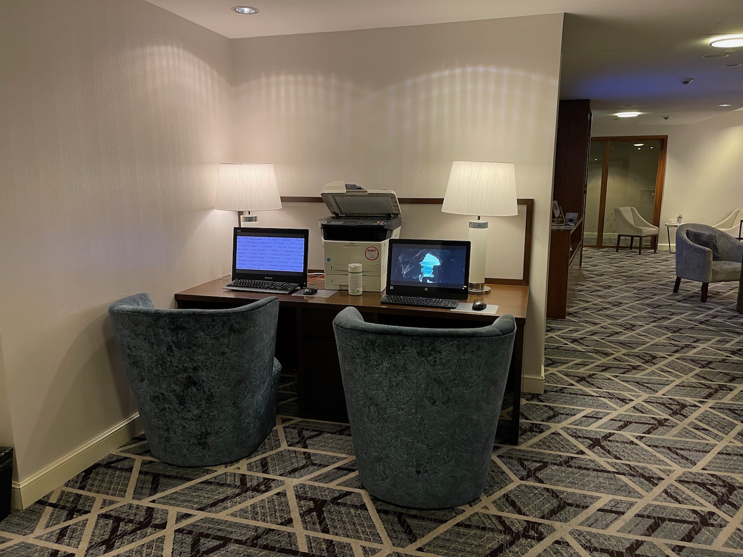 a desk with two laptops and chairs in a room with a lamp