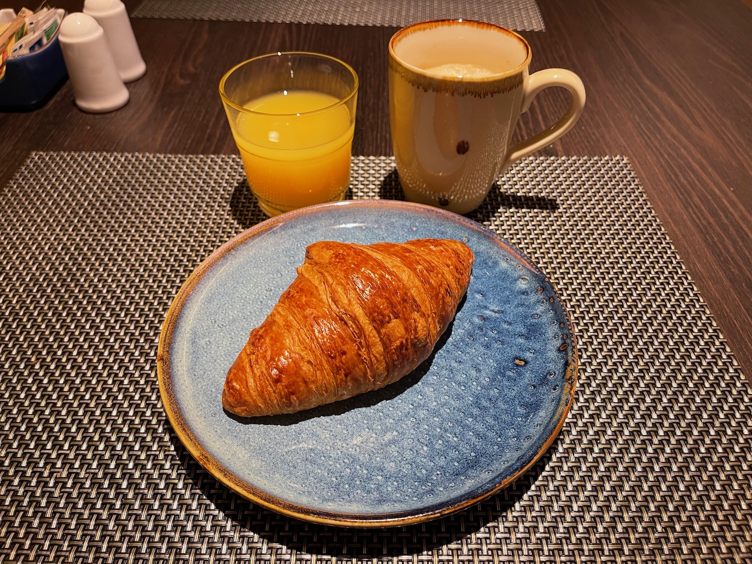 a croissant on a plate next to a mug of juice