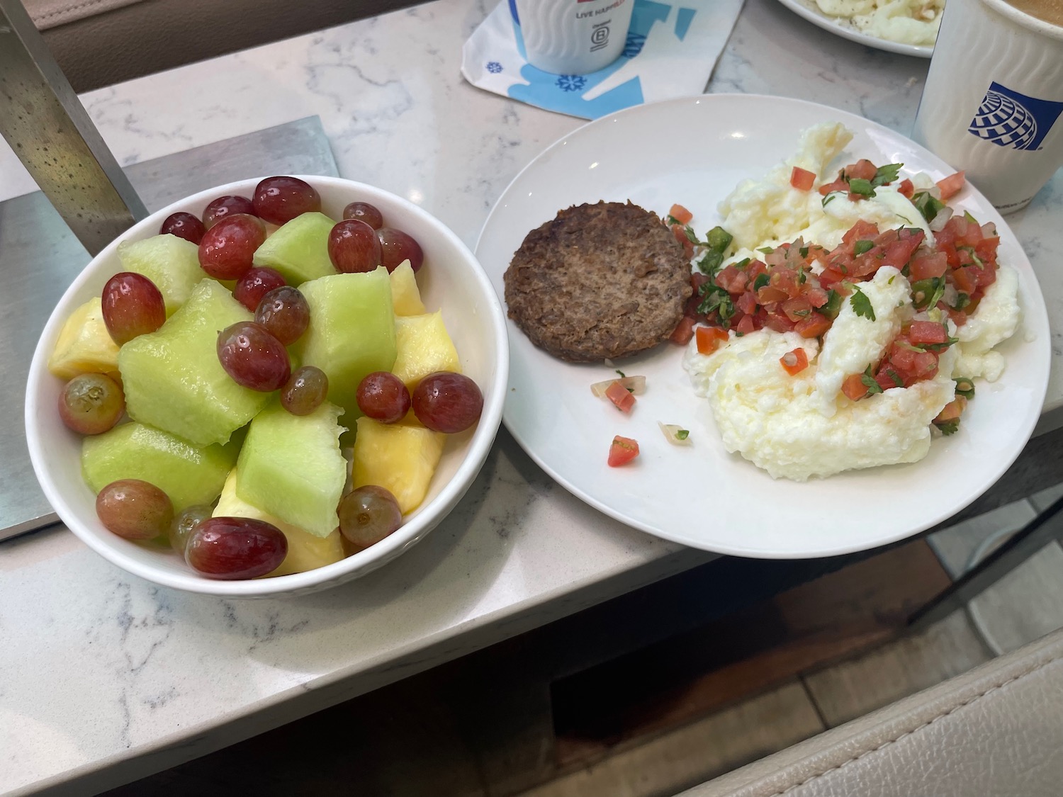 a bowl of fruit and a plate of eggs and a cutlet on a marble table