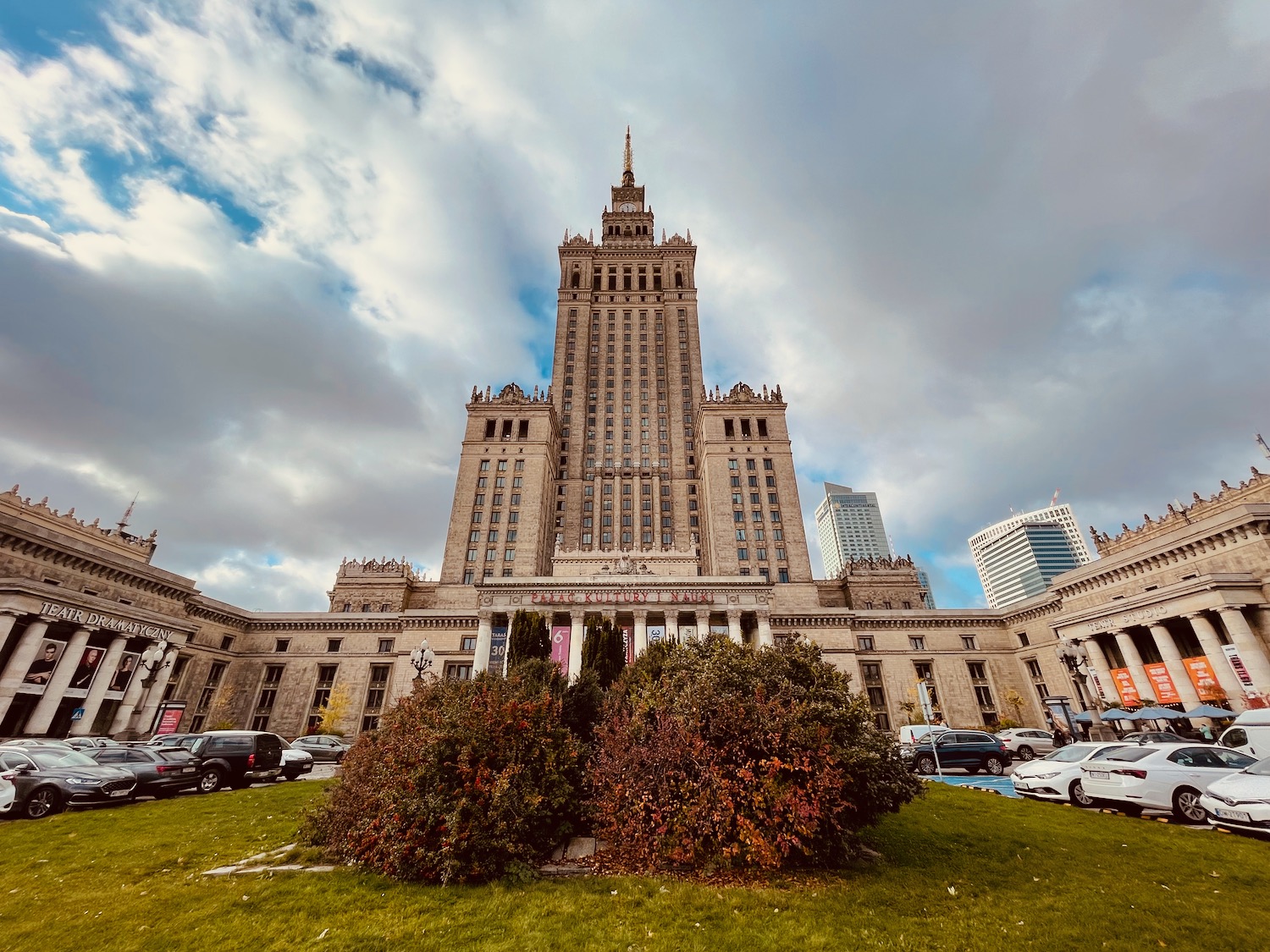 a large building with a tall tower and a lawn with cars parked in front