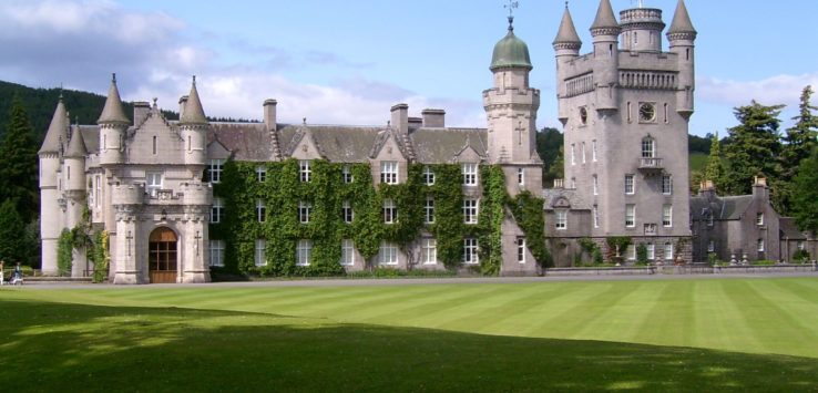 a large castle with a lawn and a flag on top with Balmoral Castle in the background