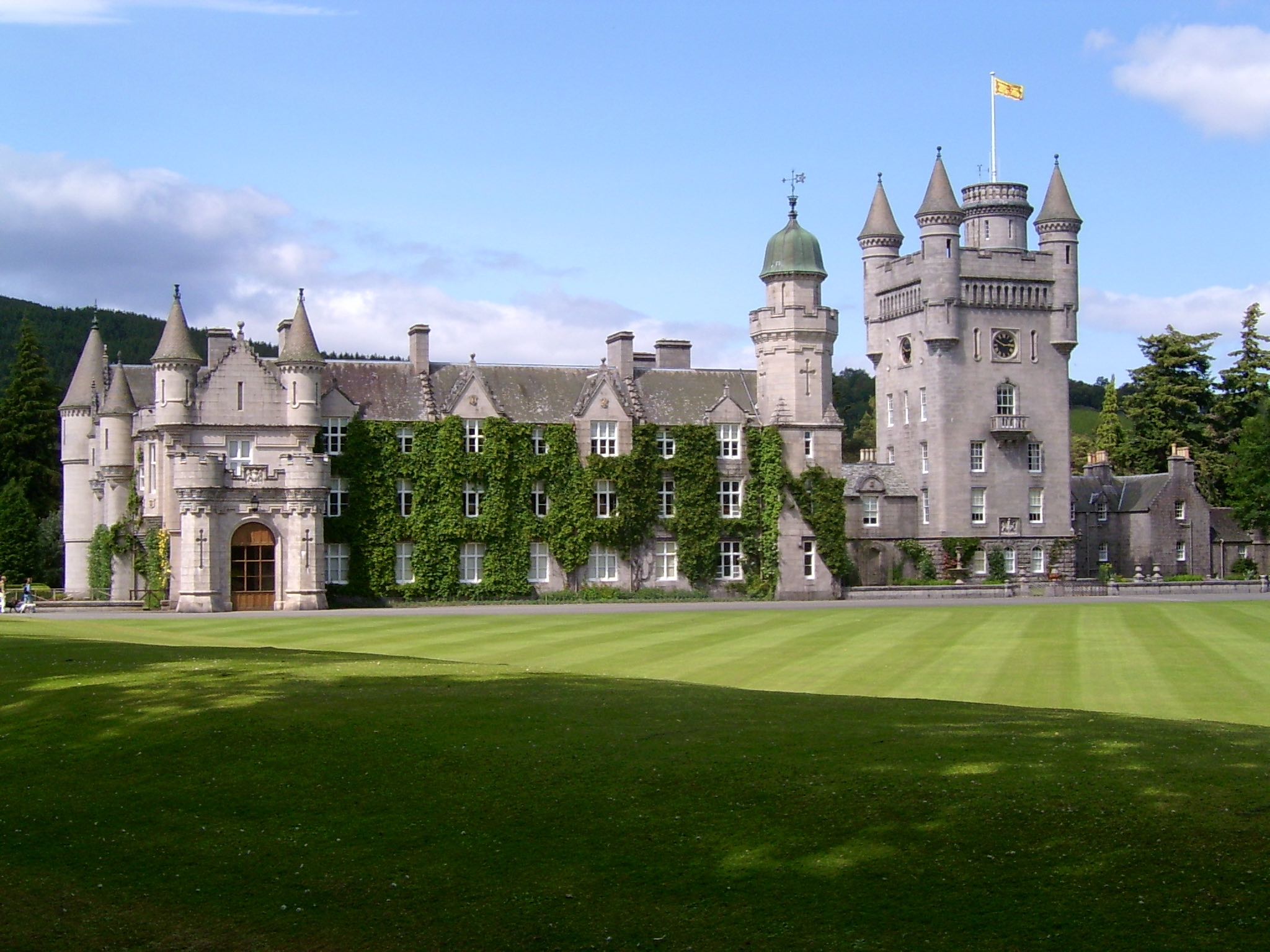 a large castle with a lawn and a flag on top with Balmoral Castle in the background