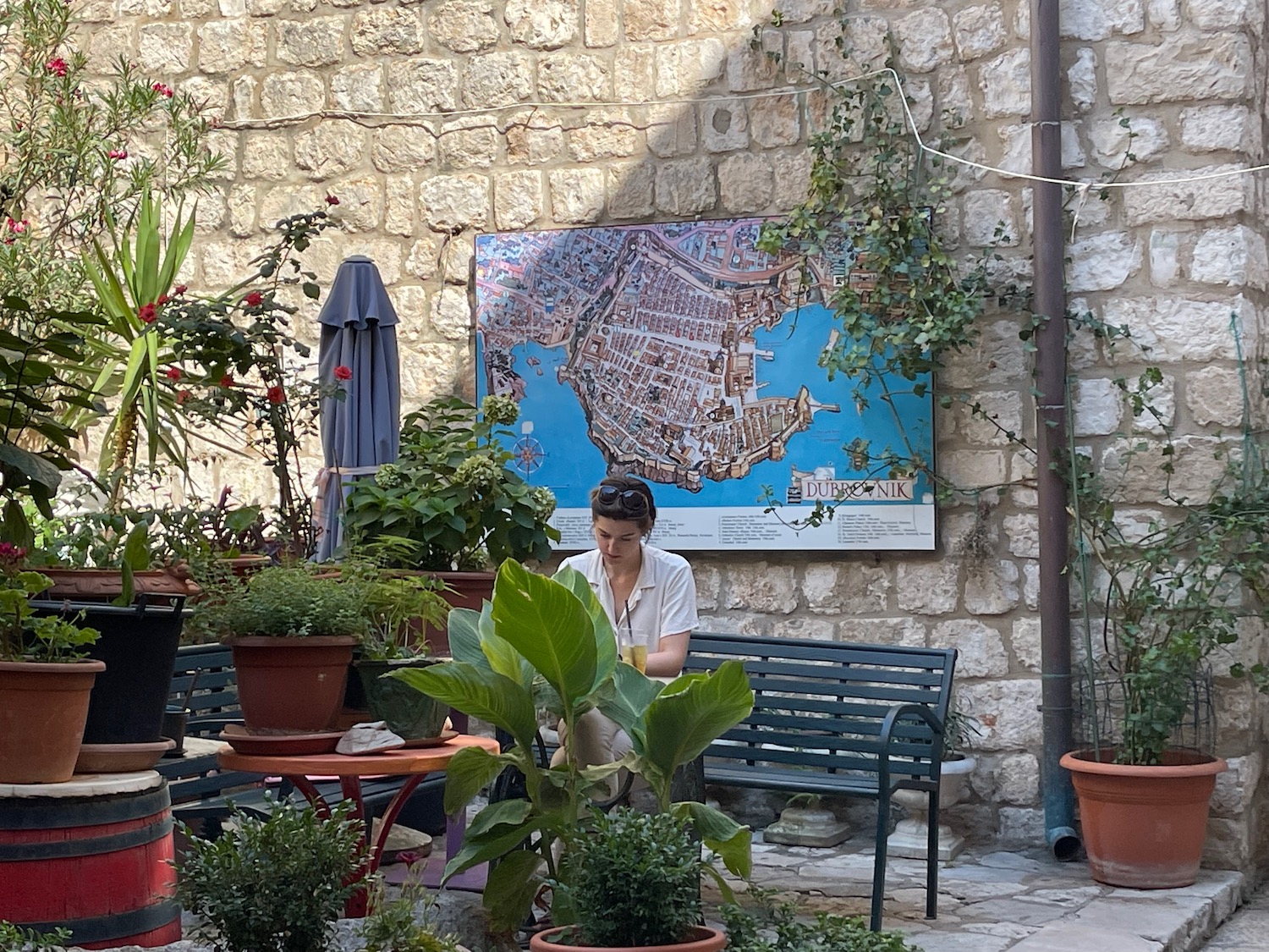 a woman sitting in a courtyard with plants and a map on the wall