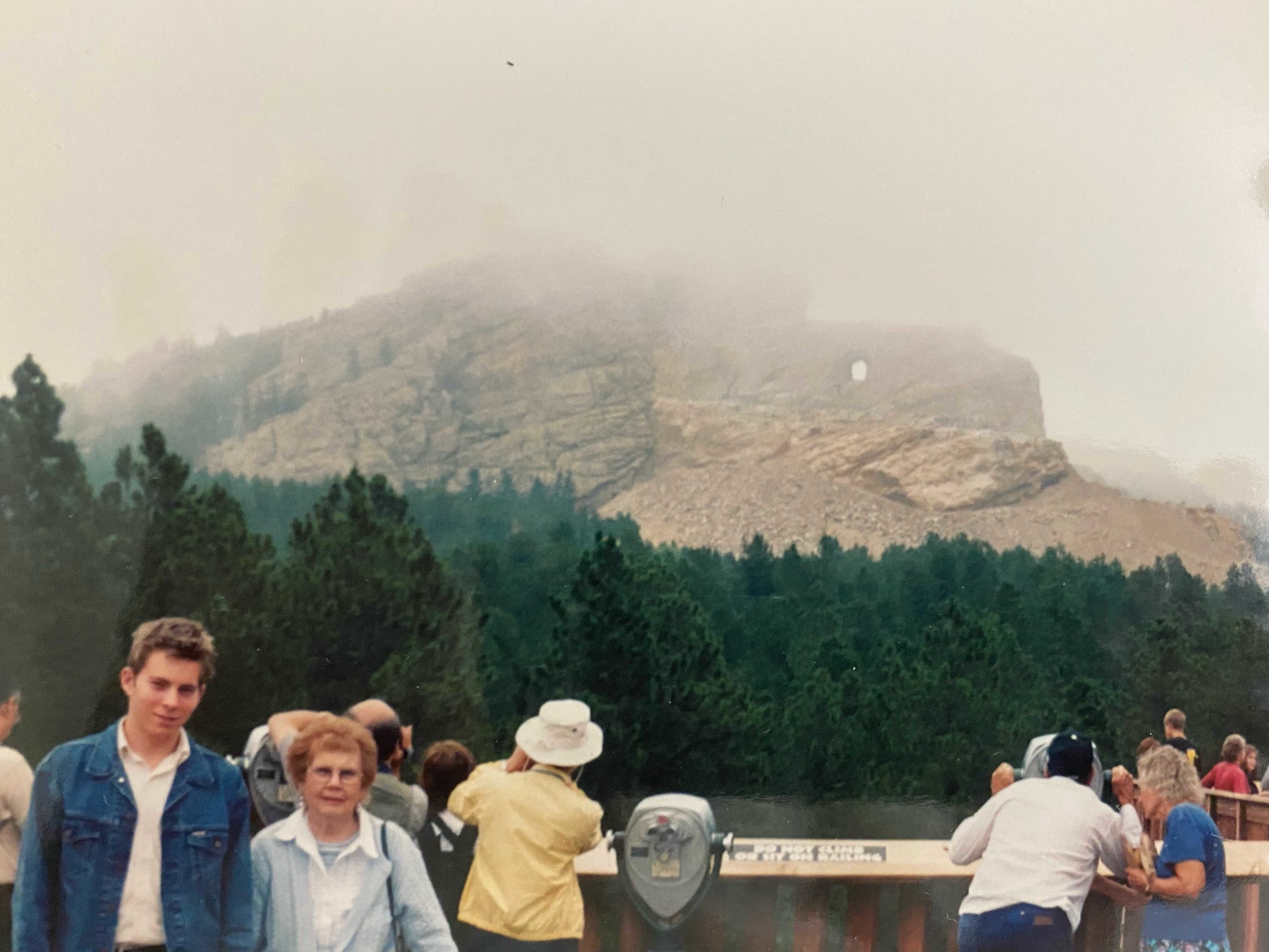 a group of people standing on a bridge with trees and mountains in the background