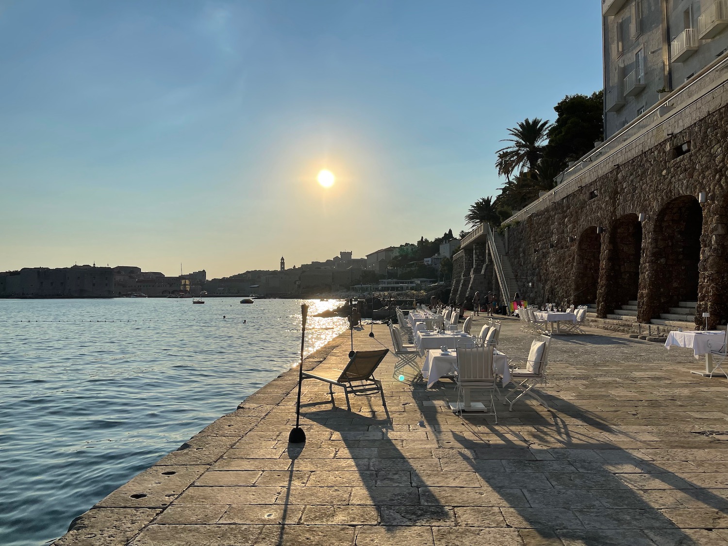 a sidewalk with tables and chairs on it by a body of water