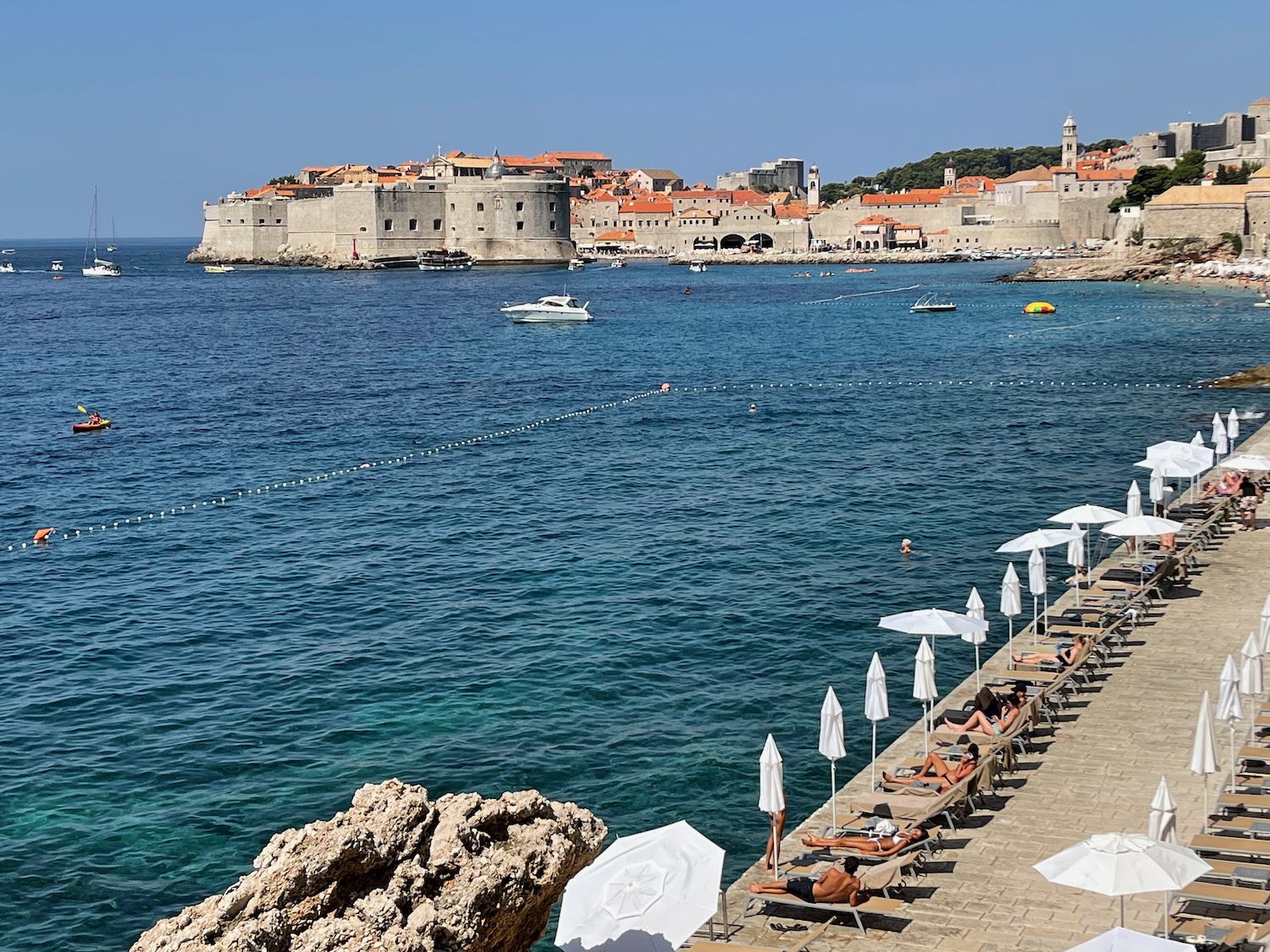a beach with a stone walkway and a large building in the background with Dubrovnik in the background