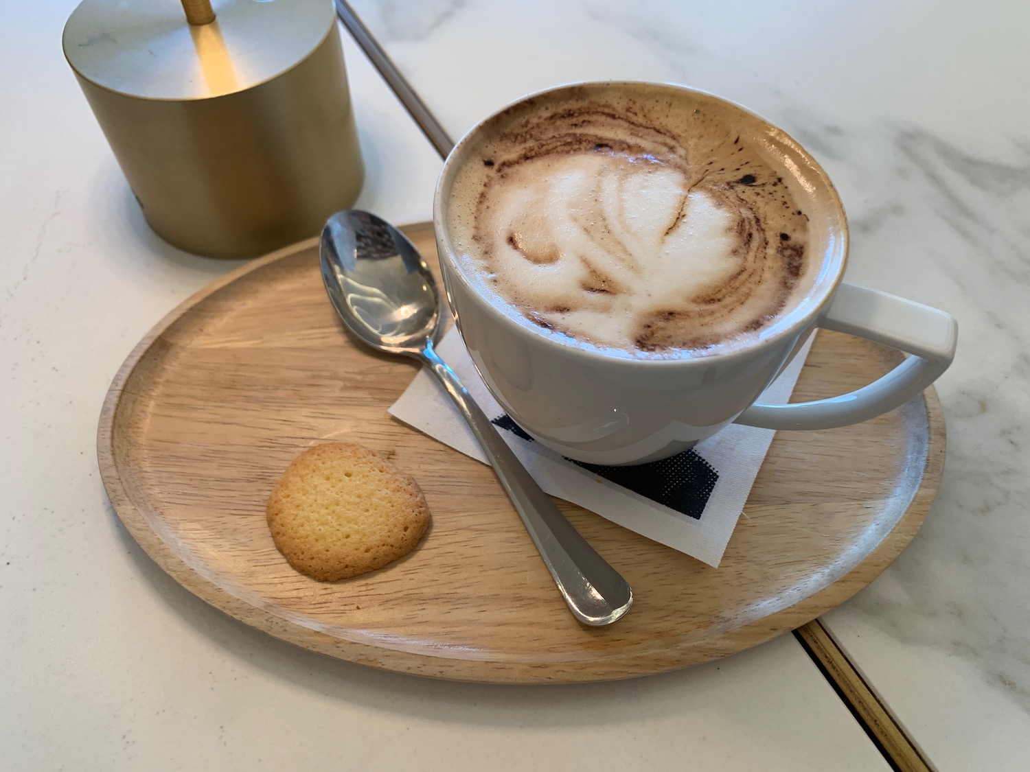 a cup of coffee with a spoon and a cookie on a wooden plate
