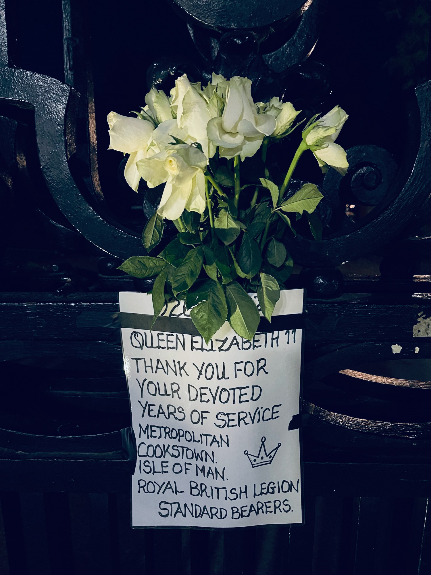 a bouquet of white roses with a sign on a black fence