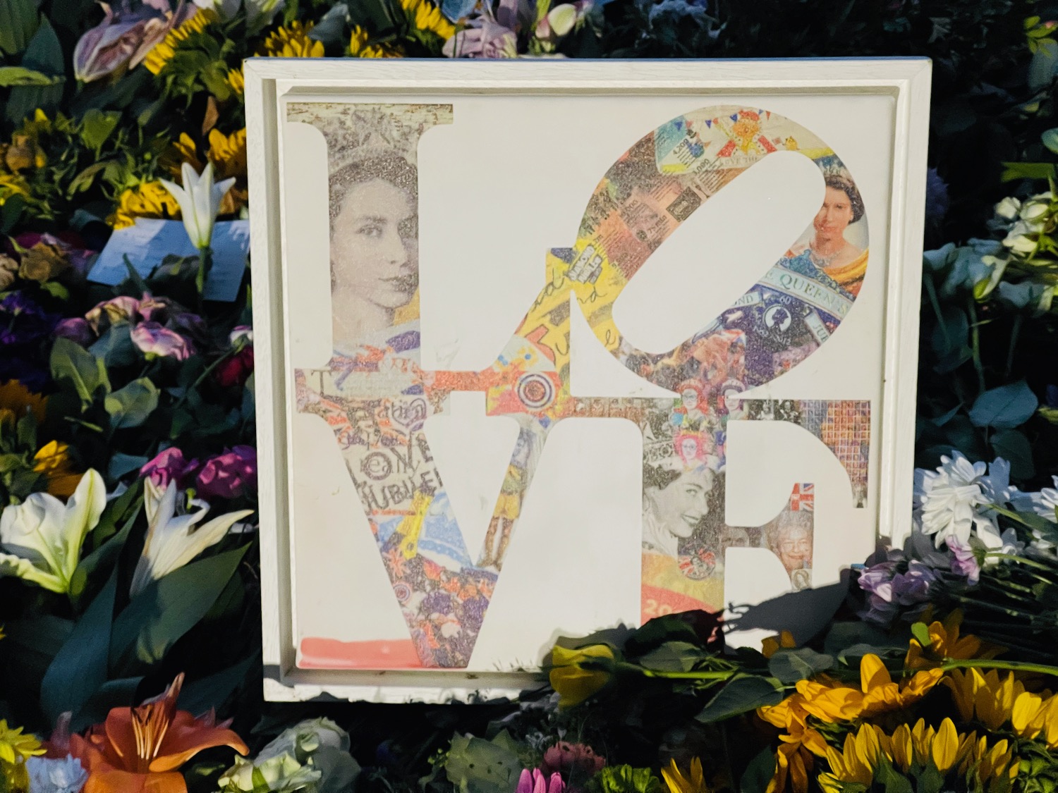 a white square sign with a word on it surrounded by flowers