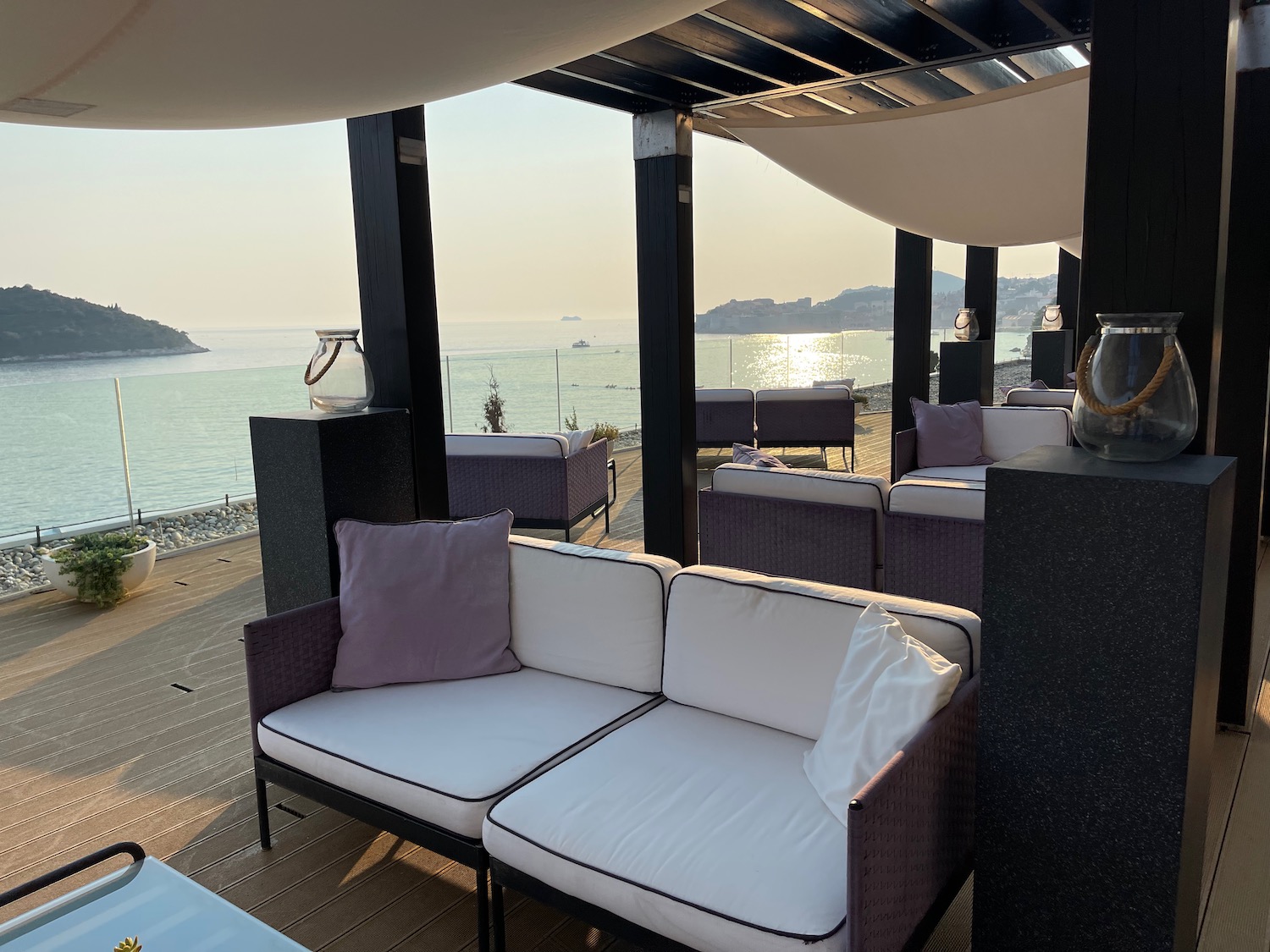 a patio with white couches and chairs on a deck overlooking water