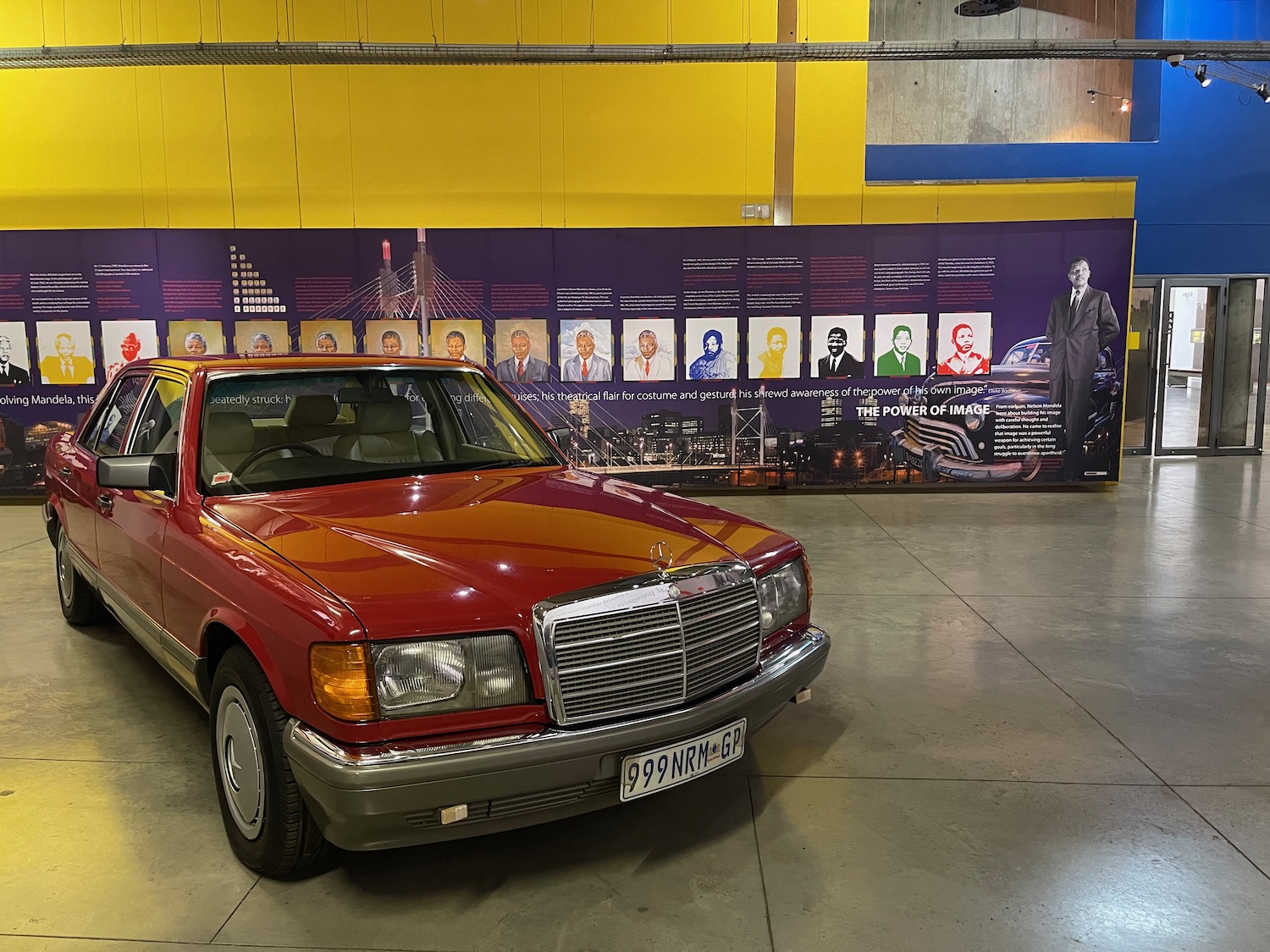 a red car in a room with a yellow wall and a poster