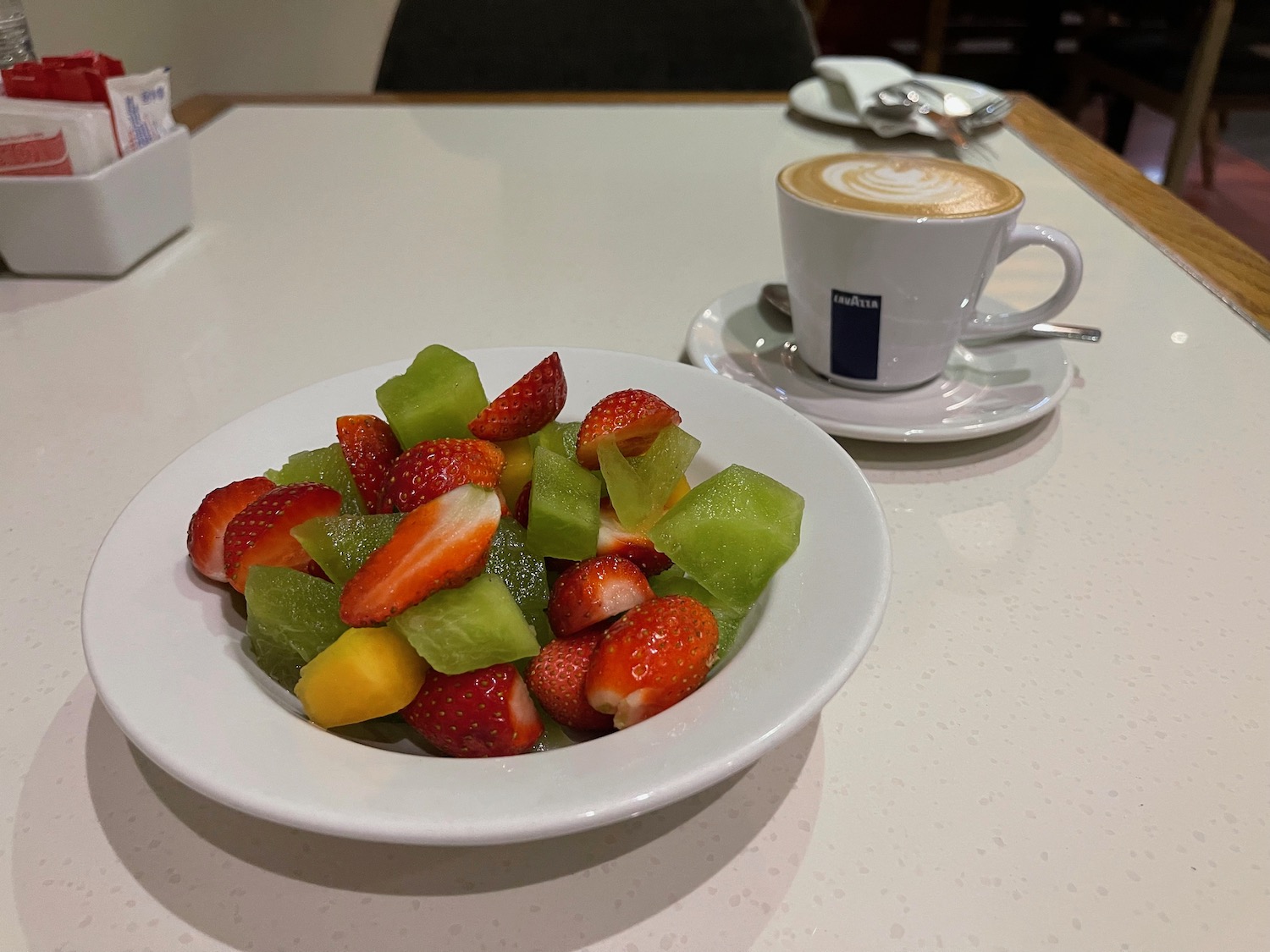 a bowl of fruit on a white plate next to a cup of coffee