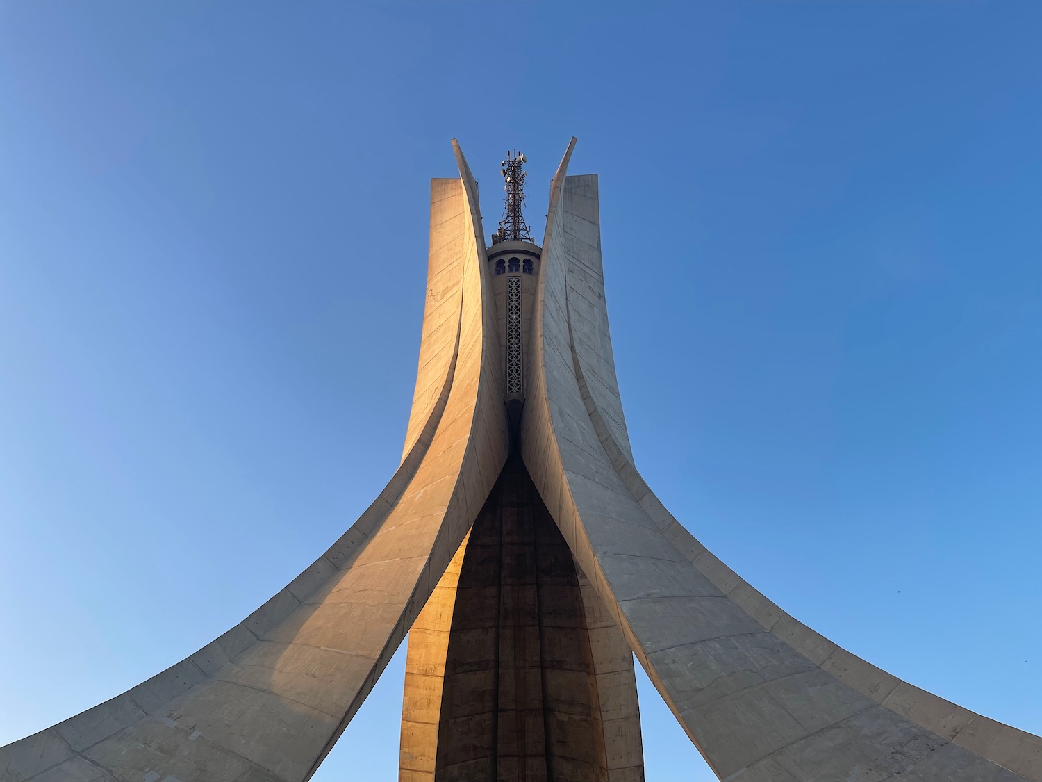 a large concrete structure with a cross on top with Martyrs' Memorial, Algiers in the background