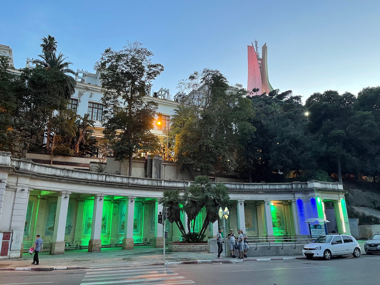 a building with columns and trees and people walking by