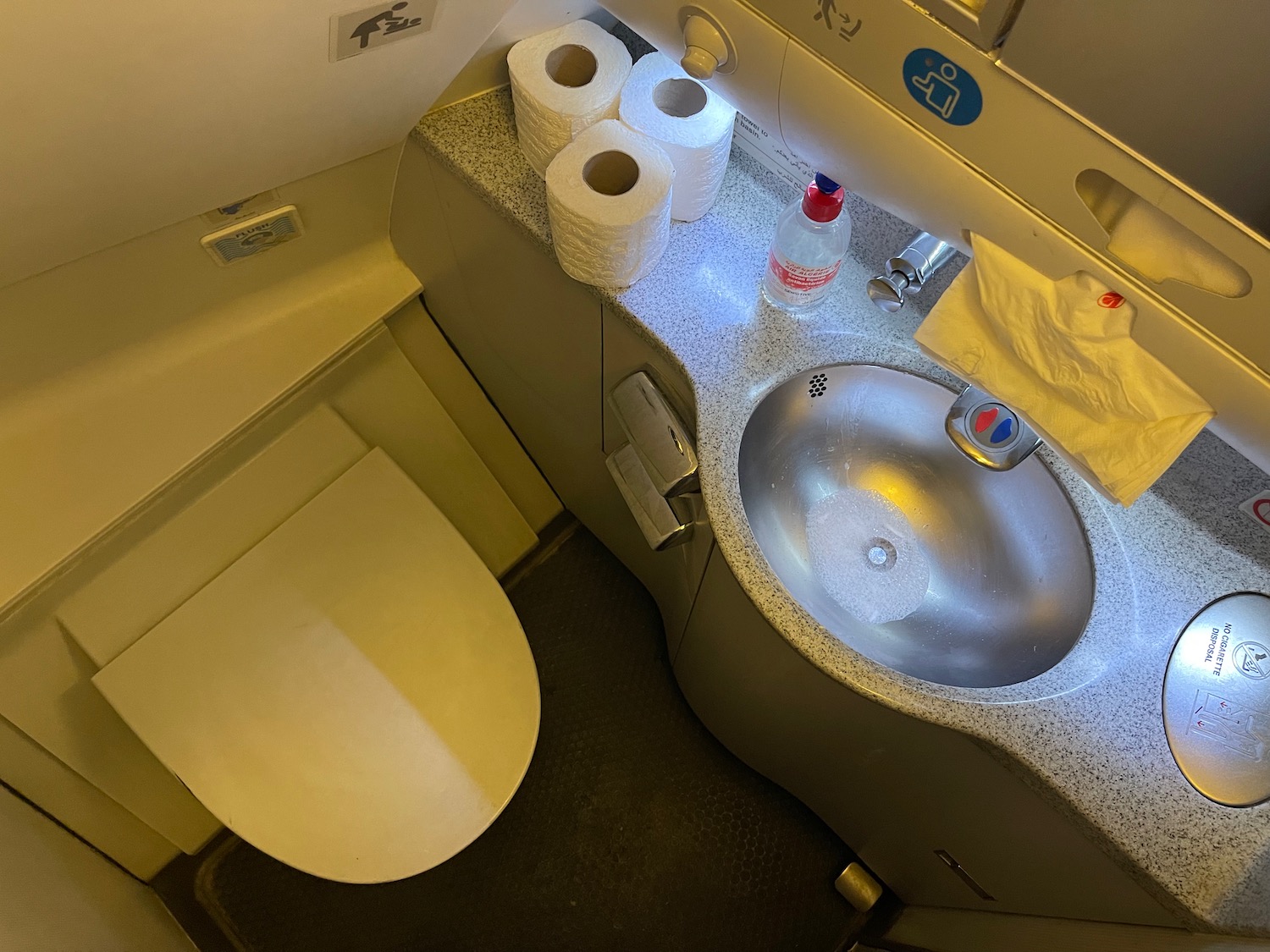 a toilet and sink with toilet paper and a bottle of water