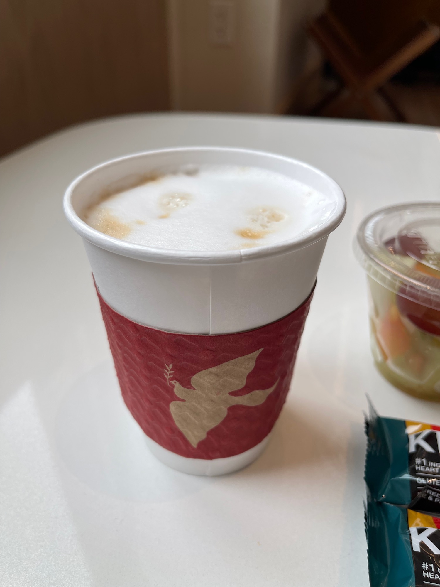 a cup of coffee with a red cover and a small container of food